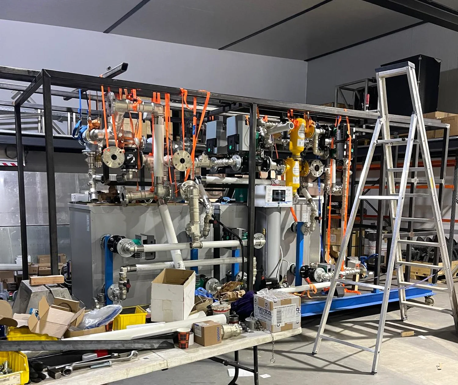 De eerste unit in aanbouw in de werkplaats: stalen frame, leidingwerk met spanbanden, warmtepompen en buffervaten
